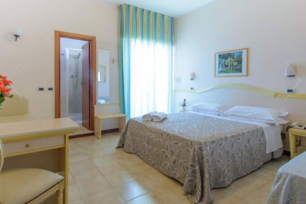 Habitación de hotel con cama, escritorio, silla, una mesita y ventana con cortinas.
