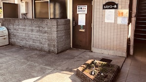 A building entrance with a tiled wall, a door with a sign, and a small garden area with flowers. - Nishijin-IVY Bunk bed twin (Kyoto)