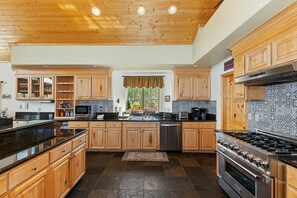 A spacious kitchen with wooden cabinets, a black countertop, a stainless steel stove, and a tiled backsplash.