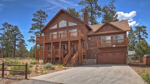A two-story log cabin with a balcony, a garage, and a stone foundation. - Sky View Lodge by Destination Big Bear : Incredible Sky Valley Estates Offering Panoramic Meadow & Mountain Views! Spa! (Big Bear City)