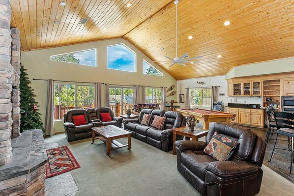 A spacious living room with leather sofas, a fireplace, and a large window overlooking a deck.