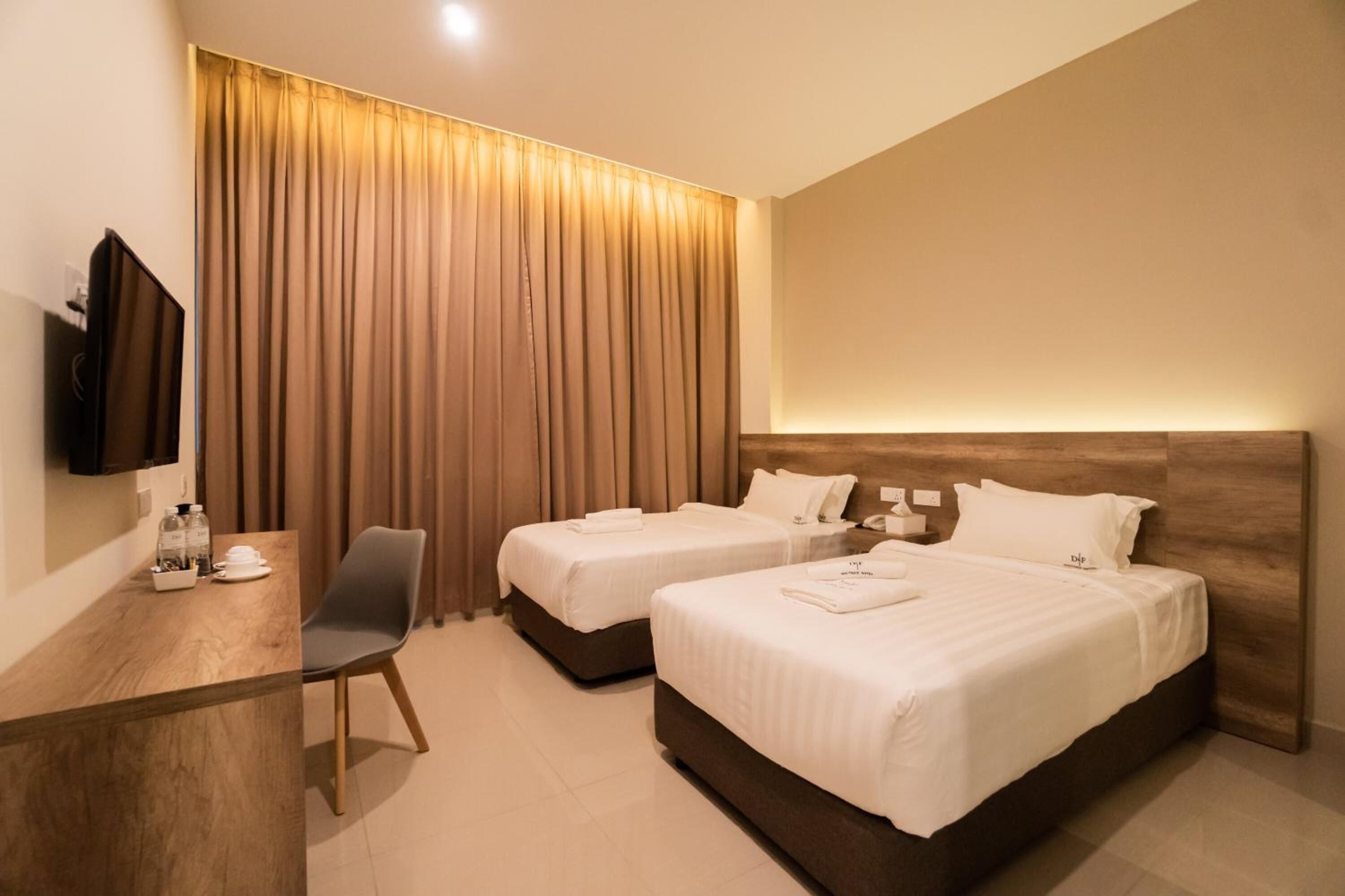 A hotel room with two beds, a desk, a chair, and a TV.