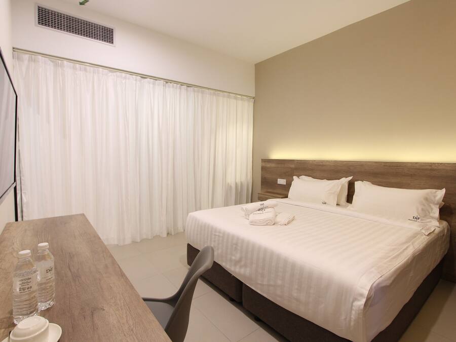 A hotel room with a bed, a desk with a chair, a TV, and a window with curtains.