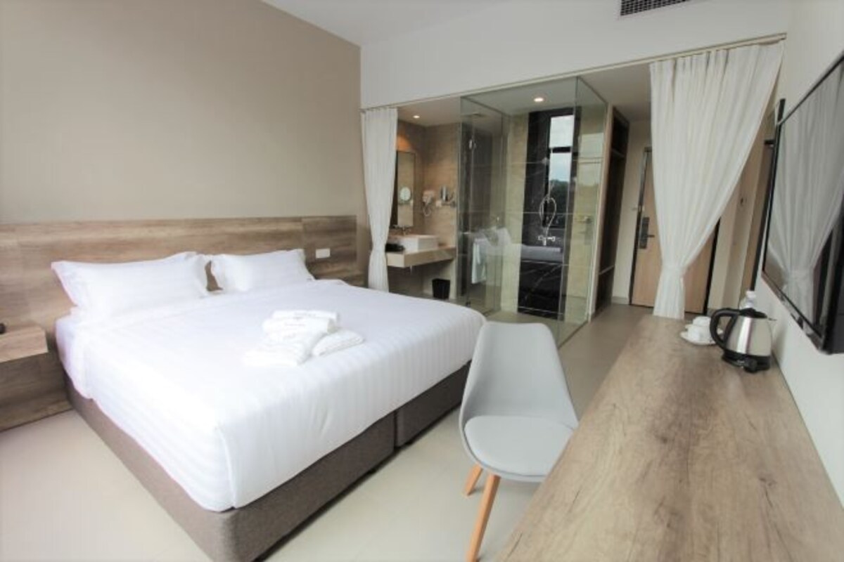 A modern hotel room with a large bed, a bedside table, a chair, and a glass-enclosed shower area.