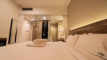 A hotel room with a large bed, a wooden headboard, a bathroom with a glass shower enclosure, and a mirror.