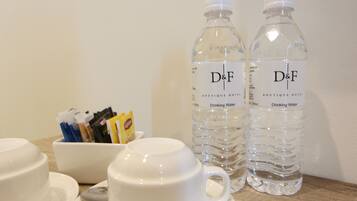 Una mesa con dos botellas de agua con la marca D&F, una taza blanca y un cuenco con sobres de café.