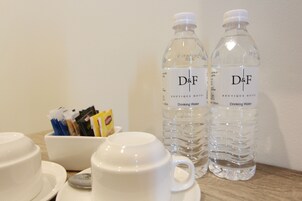 Una mesa con dos botellas de agua con la marca D&F, una taza blanca y un cuenco con sobres de café.