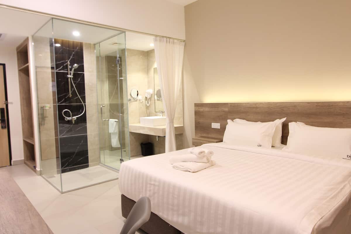 A hotel room with a glass-enclosed shower, a bed with neatly folded towels, and a wooden headboard.