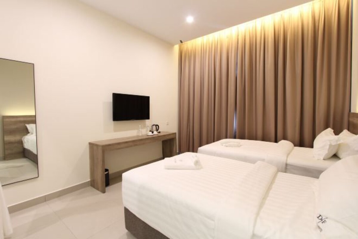 A hotel room with two beds, a flat-screen TV, a wooden desk, and a large window with curtains.