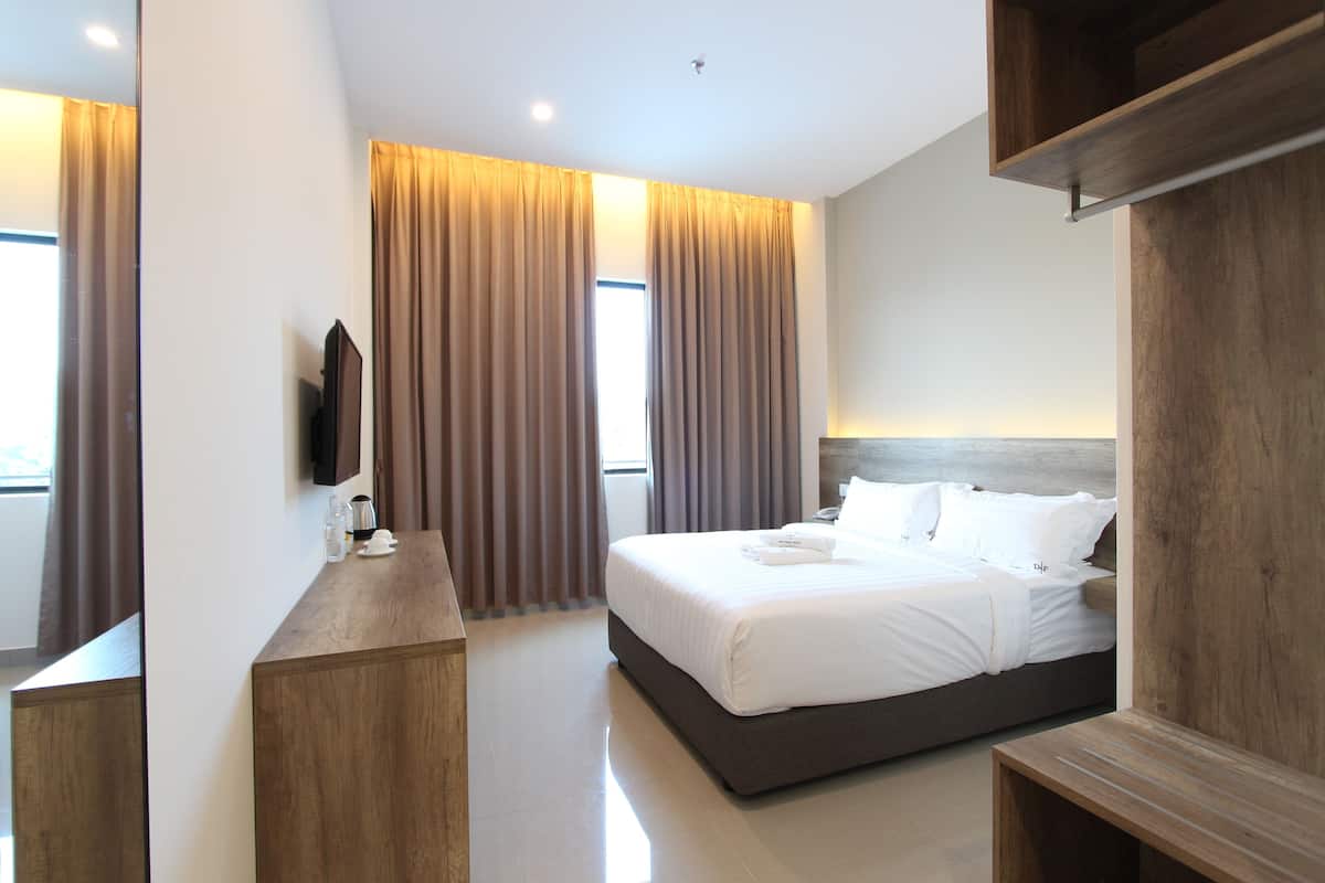 A modern hotel room with a large bed, wooden headboard, a flat-screen TV mounted on the wall, and a wooden desk.