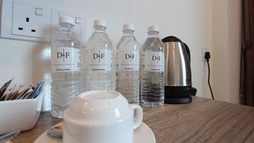 A table with a cup, saucer, and four water bottles labeled 'D&F' with 'BOUTIQUE HOTEL' and 'Drinking Water' text. There's a kettle and a power outlet in the background.