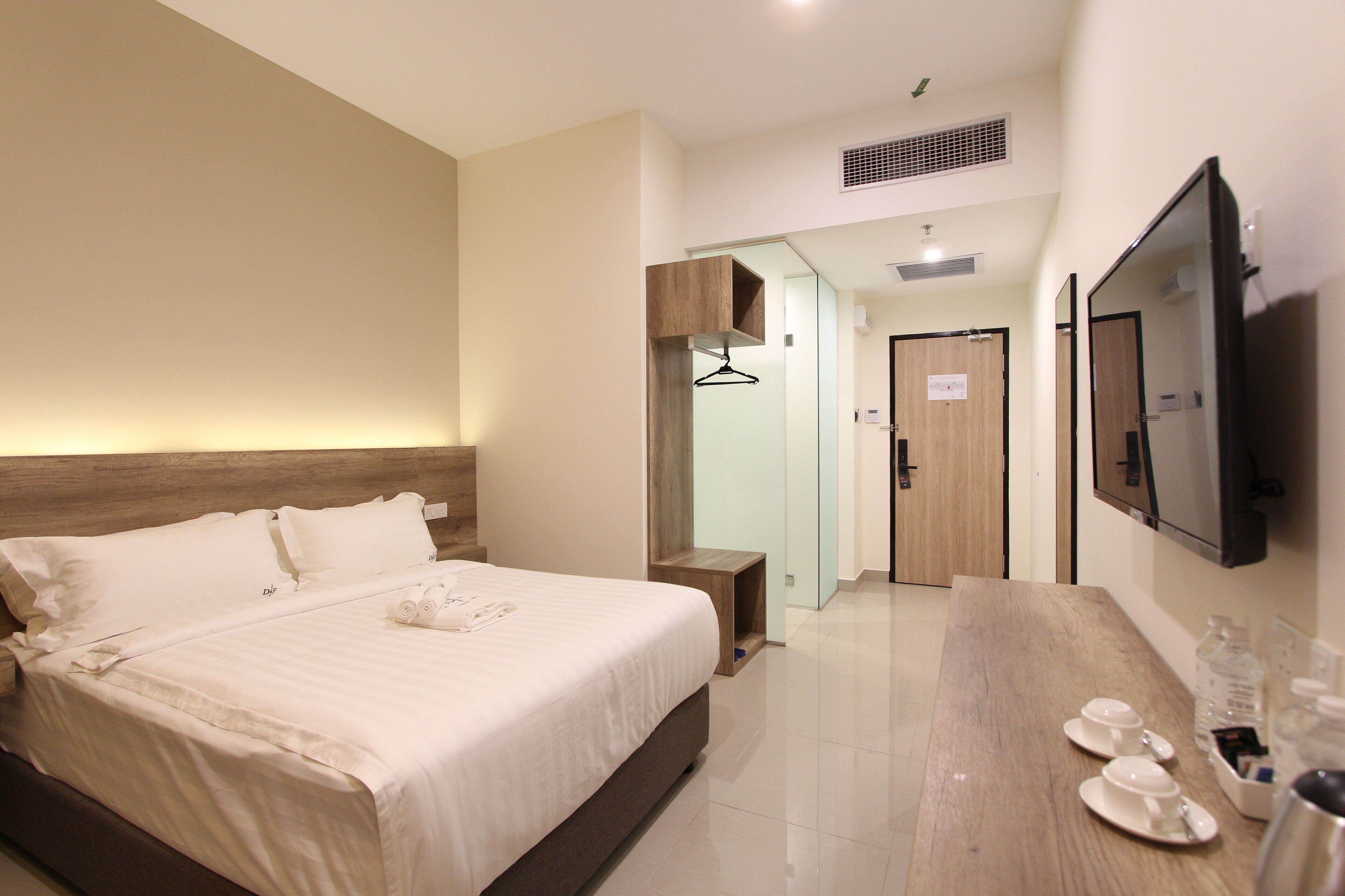 Een moderne hotelkamer met een groot bed, een houten hoofdbord, een flatscreen-tv, een houten bureau met een koffiezetapparaat en een spiegel.