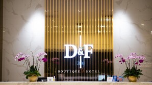 Vastaanottotiski, jossa on D&F Boutique Hotel -kyltti, kaksi ruukkuorkideaa ja marmoriseinä.