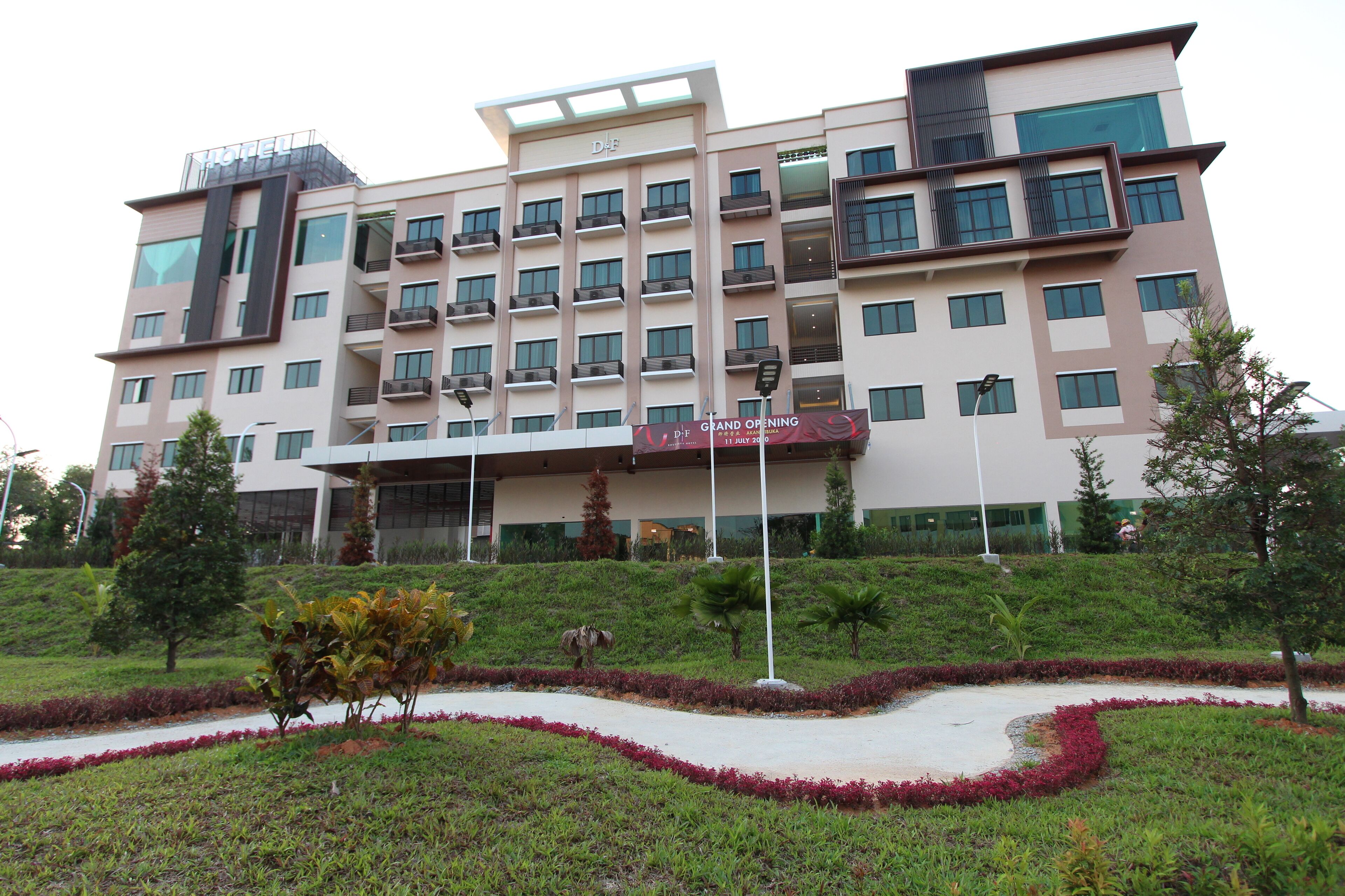 Hotel com vários andares, varandas, jardim bem cuidado e faixa de inauguração.
