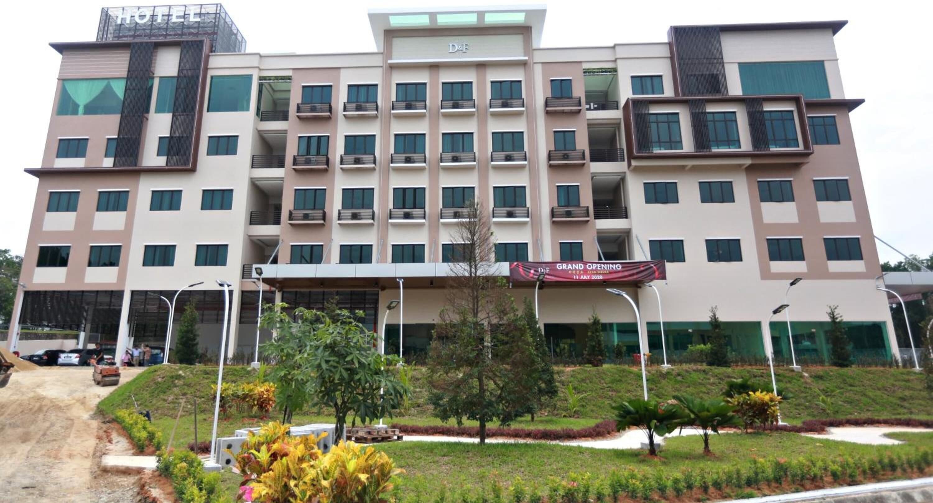 A multi-story hotel with a prominent entrance, a sign indicating a grand opening, and a landscaped garden area in front.