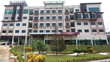 A multi-story hotel with a prominent entrance, a sign indicating a grand opening, and a landscaped garden area in front.