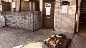 A building entrance with a tiled wall, a door with a sign, and a small garden area with flowers. - Nishijin-IVY 5 beds (Kyoto)