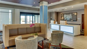 A hotel lobby with a reception desk, a sofa, and two armchairs. - Holiday Inn Express Wilmington Porters Neck by IHG (Wilmington)