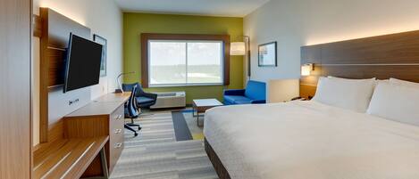 A hotel room with a large bed, a desk with a flat-screen TV, a blue chair, and a window with a view.
