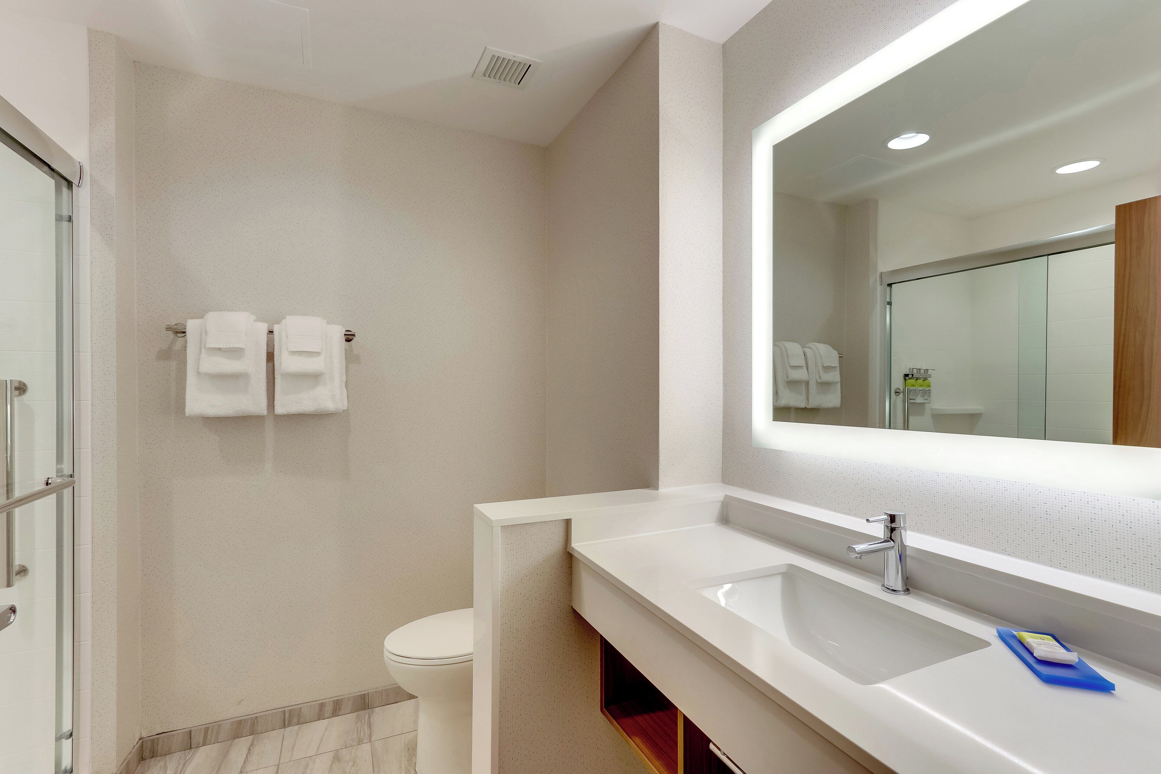 A modern bathroom with a large mirror, white sink, and a glass shower enclosure.