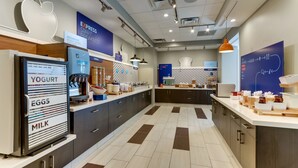 A modern kitchen with a yogurt dispenser, eggs, and milk station, a breakfast bar, and a chalkboard menu. - Holiday Inn Express Wilmington Porters Neck by IHG (Wilmington)