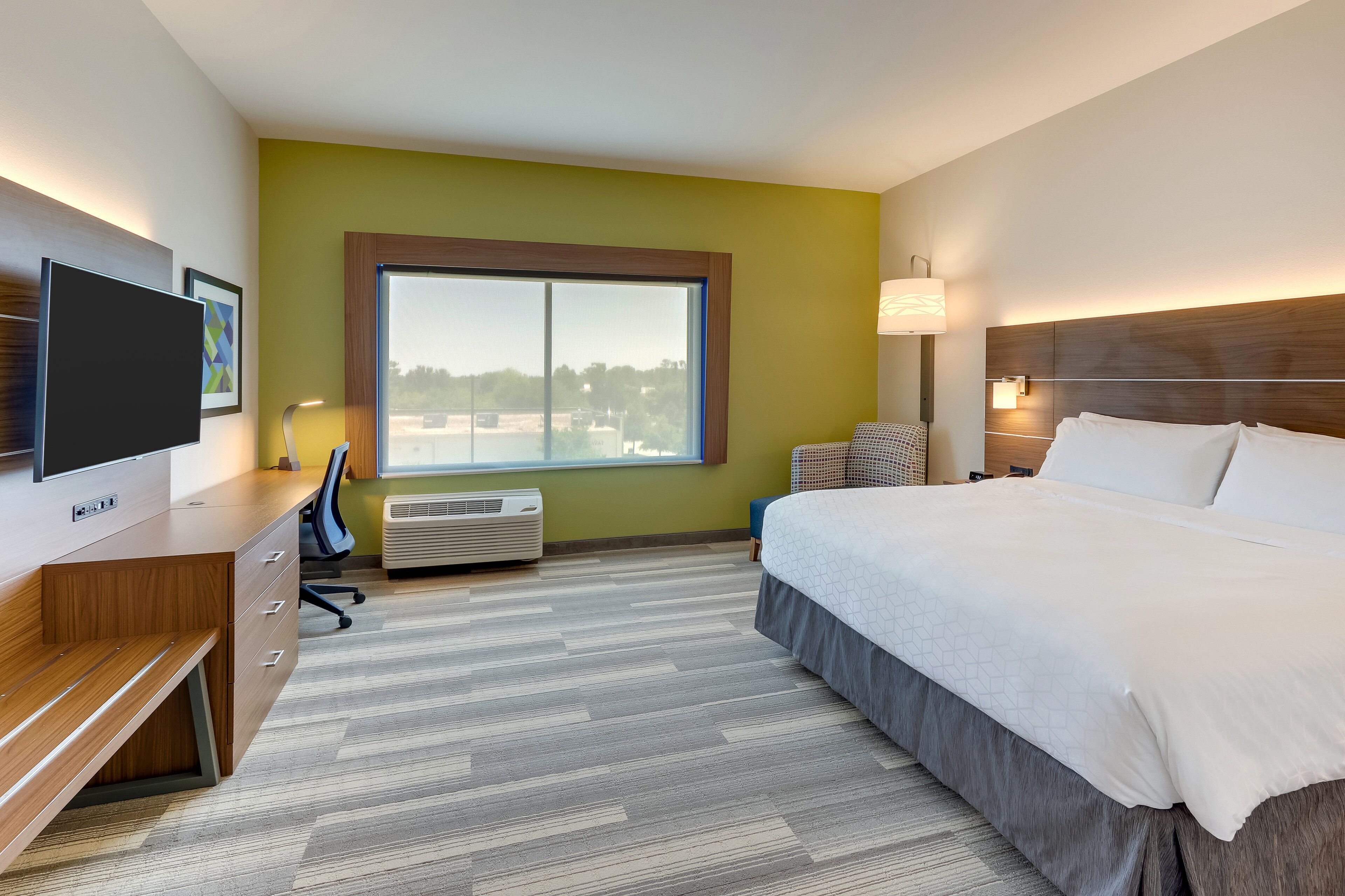 A hotel room with a bed, desk, chair, TV, and a large window.