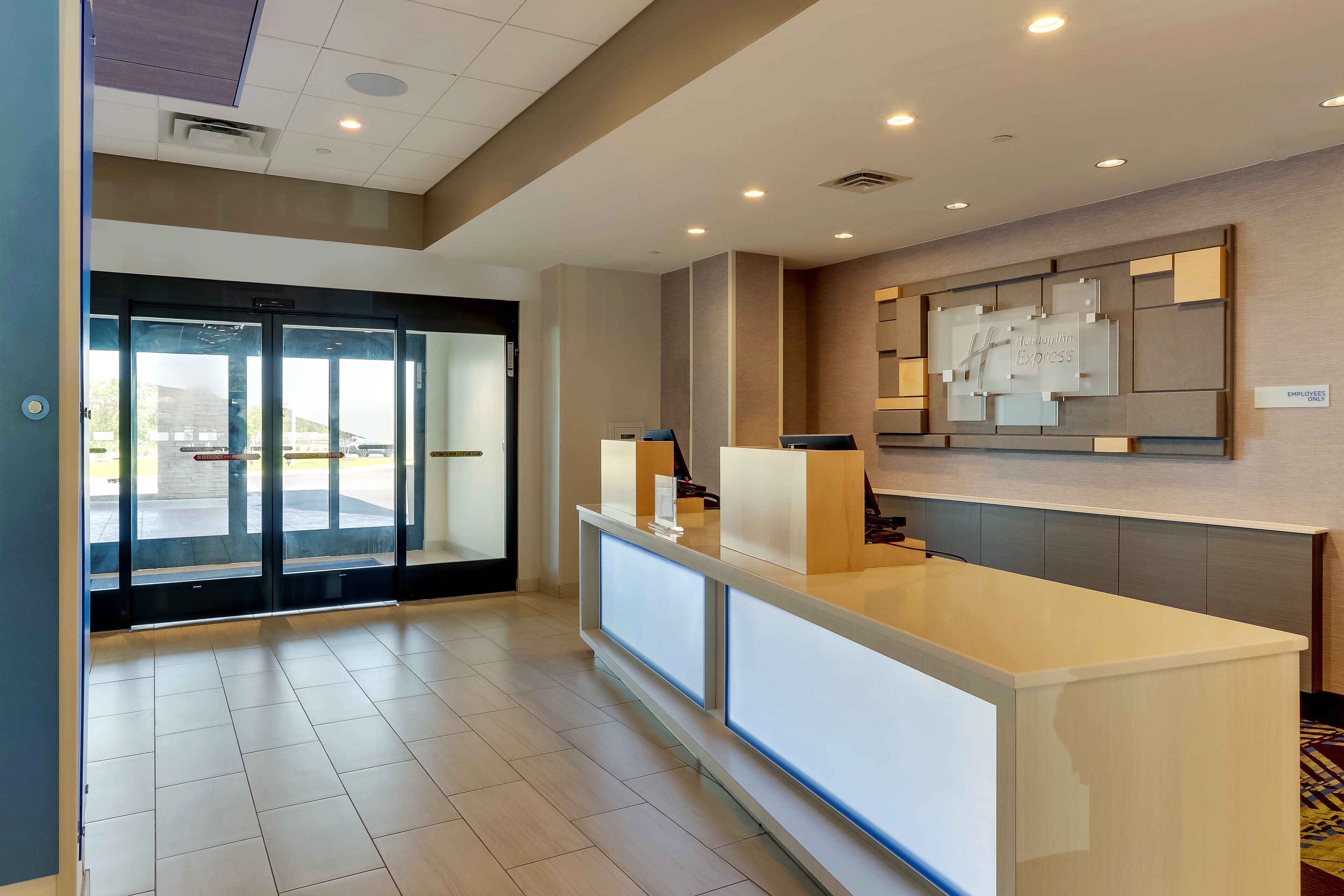 A hotel reception area with a modern design, featuring a reception desk, glass doors, and a wall-mounted information display.