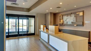 A hotel reception area with a modern design, featuring a reception desk, glass doors, and a wall-mounted information display.