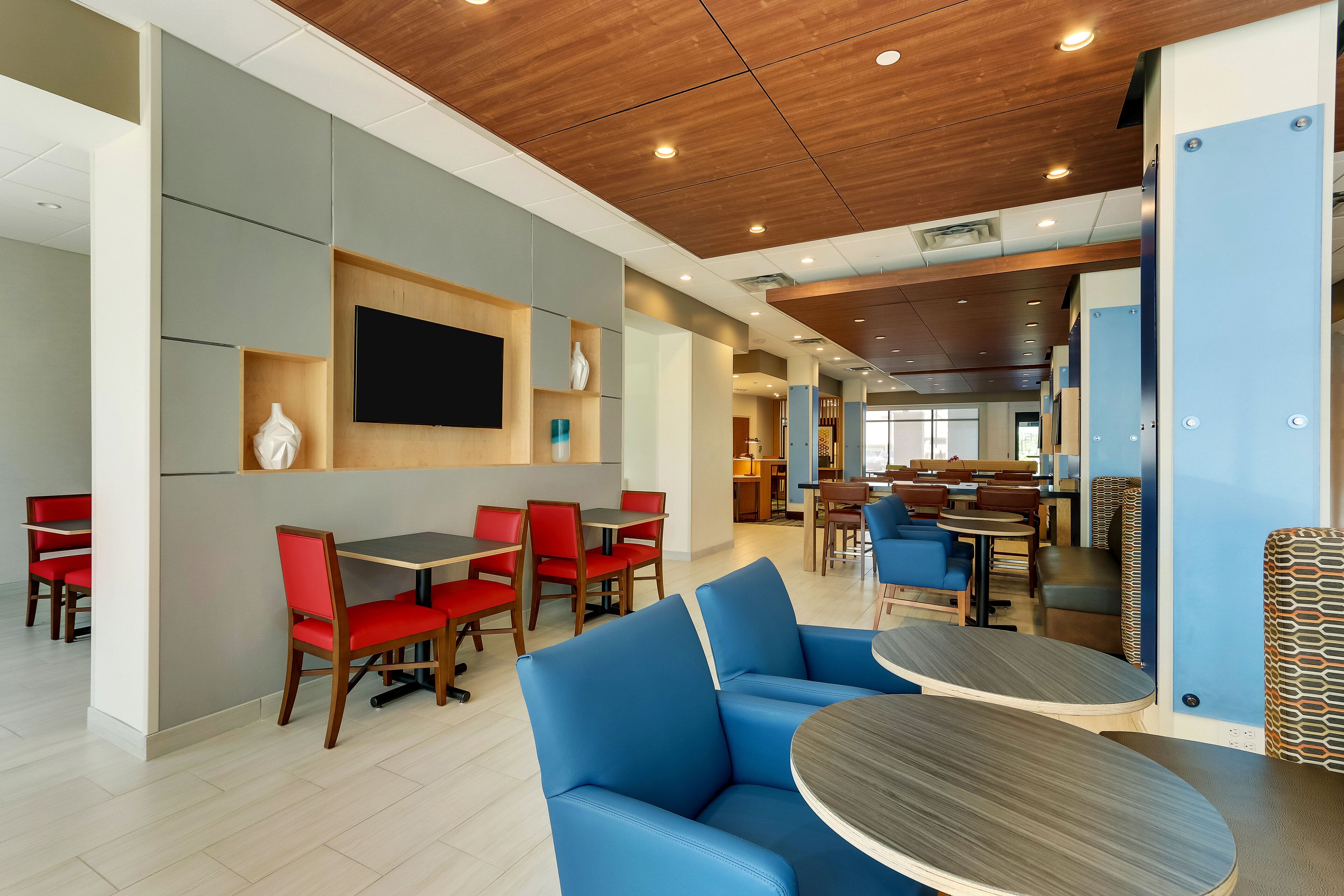 Un restaurant moderne avec des sièges rouges et bleus, un téléviseur à écran plat et un plafond en bois.