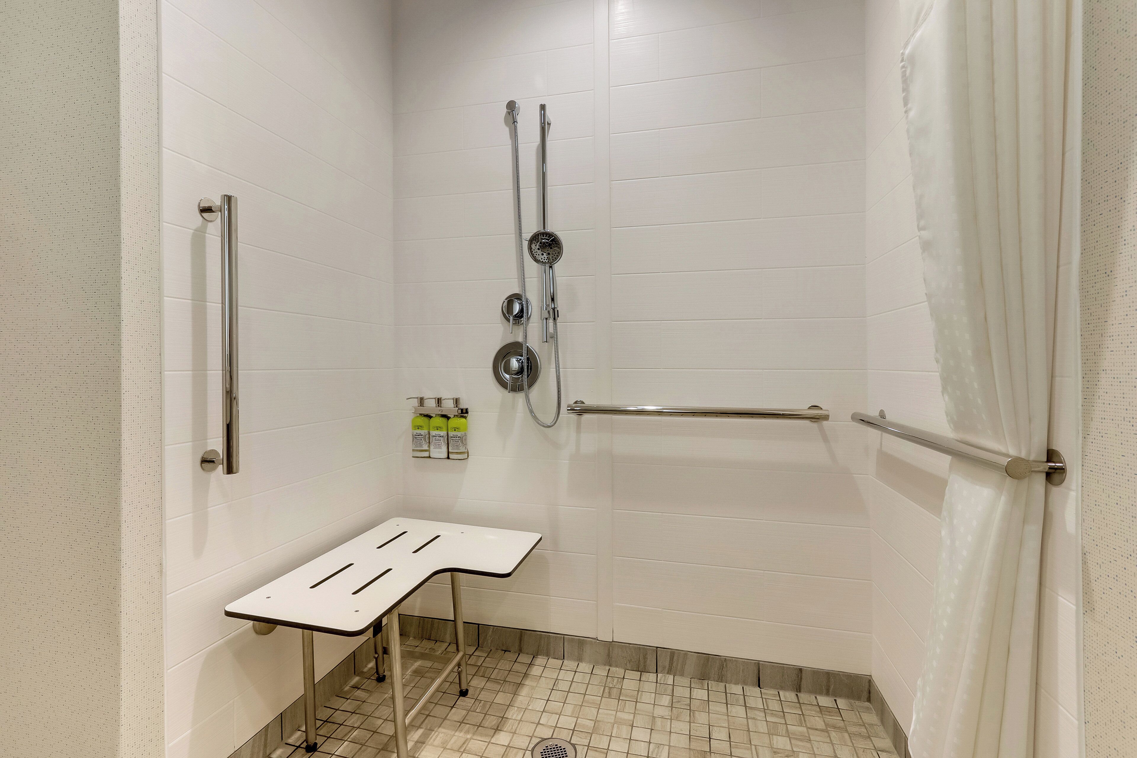 Ein kleiner, abgeschlossener Duschbereich mit einer Haltestange, einer Handbrause und einer an der Wand befestigten Handbrause.