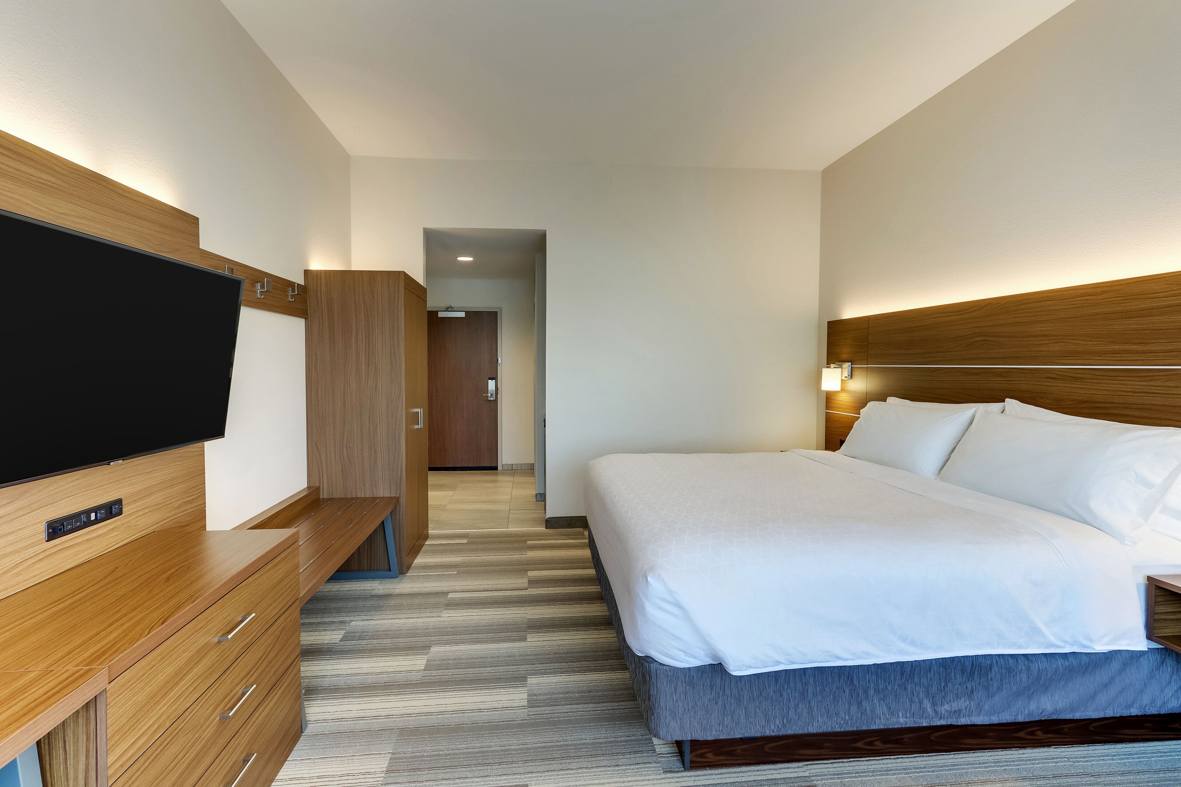 A modern hotel room with a flat-screen TV, wooden furniture, a large bed with white linens, and a wooden headboard.