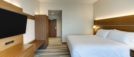 A modern hotel room with a flat-screen TV, wooden furniture, a large bed with white linens, and a wooden headboard.