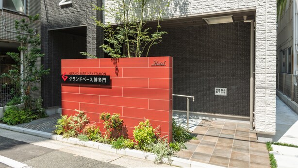 L’entrée d’un hôtel, avec une enseigne rouge indiquant « Grand Base Hakata Mon ».