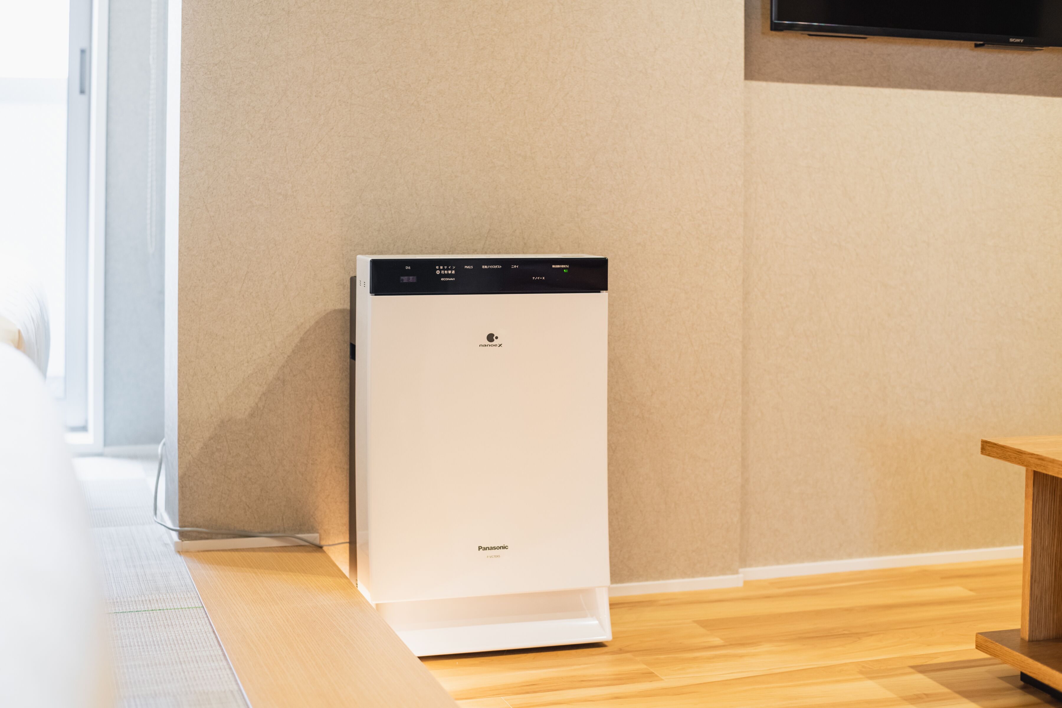A compact, white, wall-mounted appliance with a digital display, likely a microwave or small oven, in a modern kitchen setting with wooden flooring and a neutral wall color.