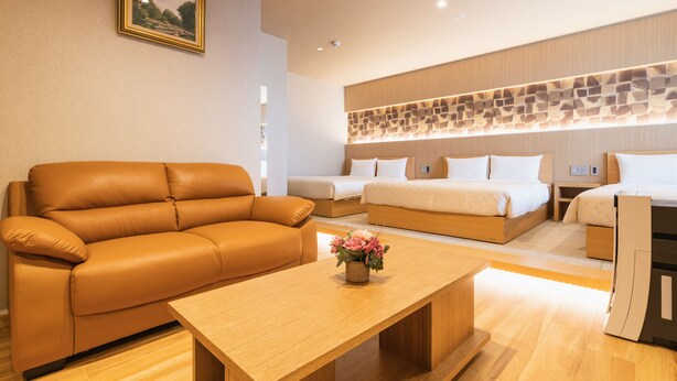 A modern hotel room with a sofa, a bed, a wooden coffee table, and a decorative wall panel. - GRAND BASE Hakatamon (Fukuoka)