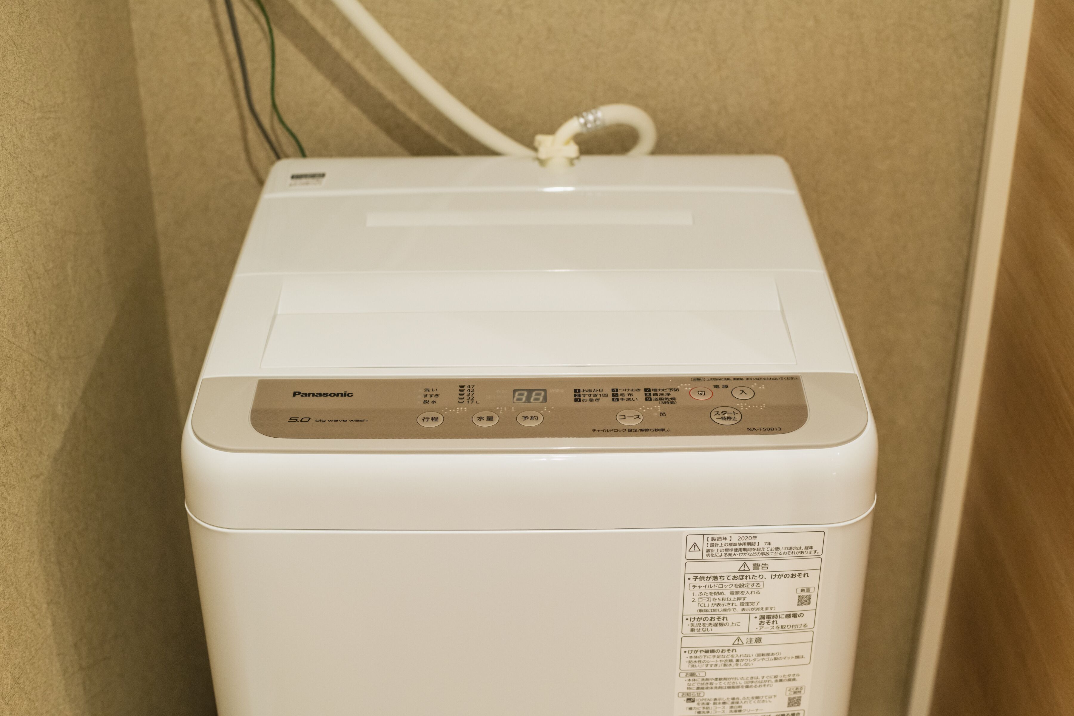 Een witte Panasonic wasmachine met een bedieningspaneel en een etiket aan de zijkant.