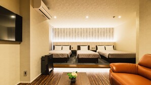 A hotel room with a flat-screen TV mounted on the wall, a wooden coffee table with a flower centerpiece, two beds with matching headboards, and a leather sofa. - GRAND BASE Hakatamon (Fukuoka)