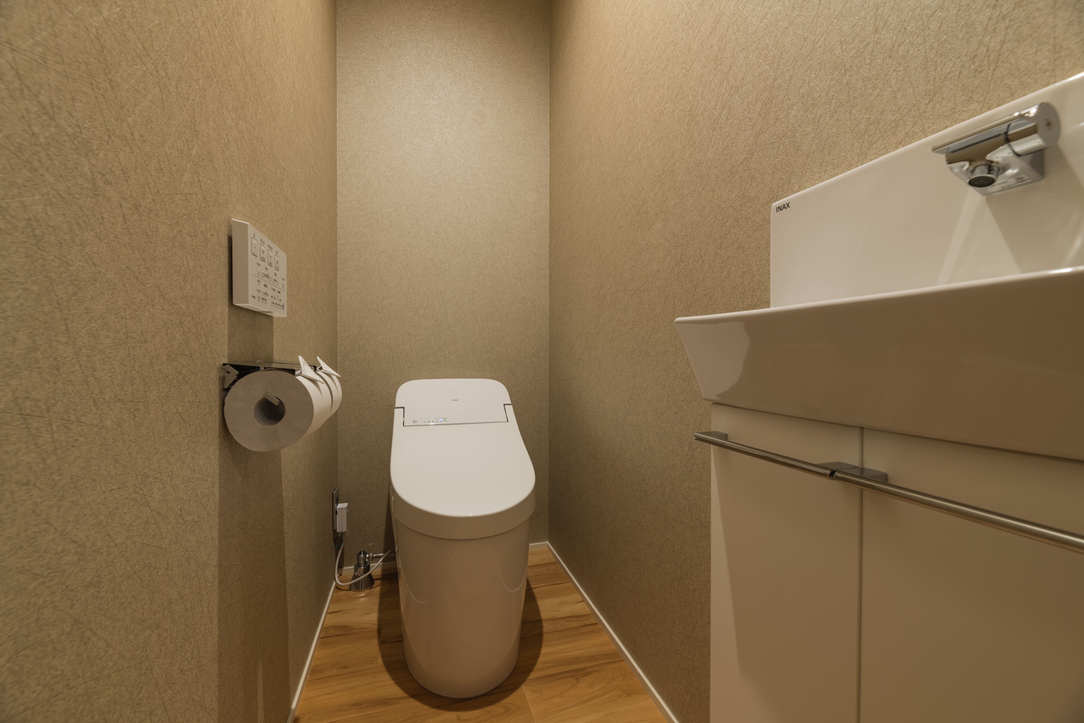 A compact bathroom with a toilet, a wall-mounted toilet paper dispenser, and a sink with a mirror.