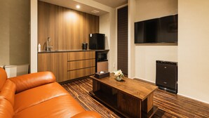 A compact living space with a kitchenette, a sofa, a coffee table, and a flat-screen TV mounted on the wall. - GRAND BASE Hakatamon (Fukuoka)