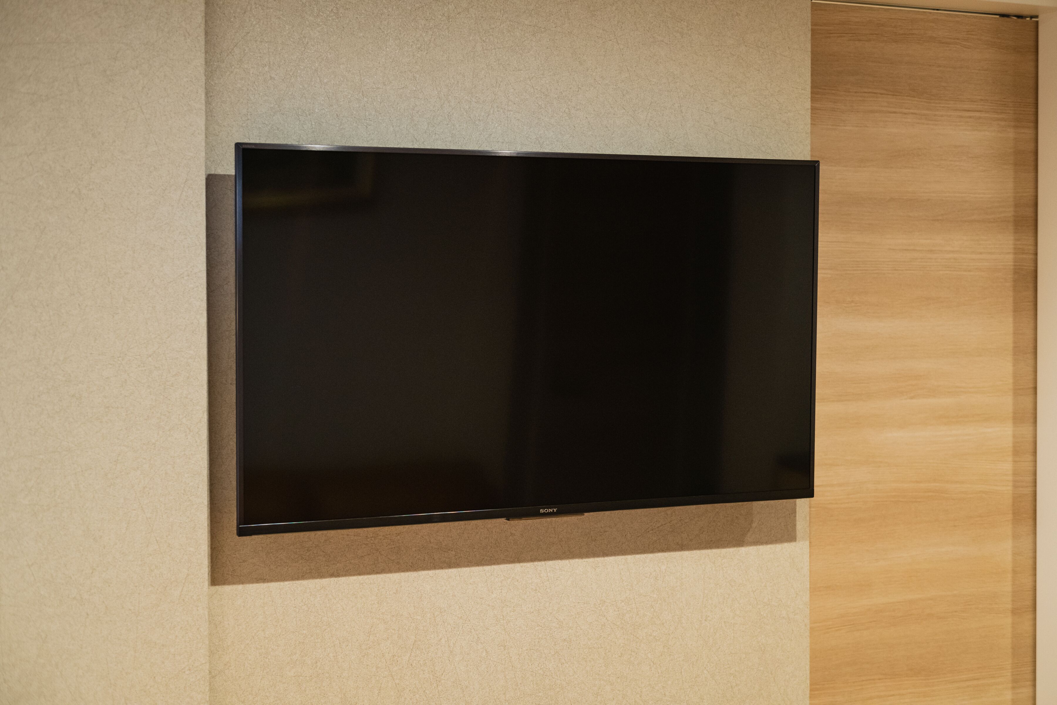 Un téléviseur à écran plat fixé au mur, avec un panneau en bois sur le côté droit.