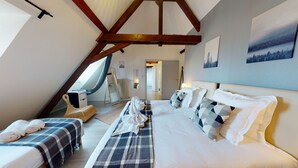 Ein gemütliches Schlafzimmer mit einem großen Bett, zwei kleineren Betten, einem gewobenen Sessel und Blick auf einen Wald durch ein Fenster.