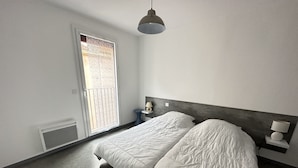 Een slaapkamer met een groot bed, een nachtkastje met een lamp, een raam met uitzicht en een plafondlamp.