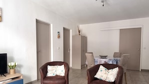 Een woonkamer met twee bruine leren fauteuils, een salontafel, een tv op een blauwe kast, en een eethoek met een tafel en stoelen.
