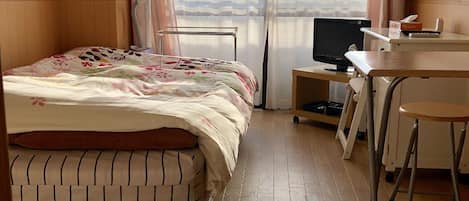 A hotel room with a bed, a desk with a computer, an air conditioner, and a window with curtains.