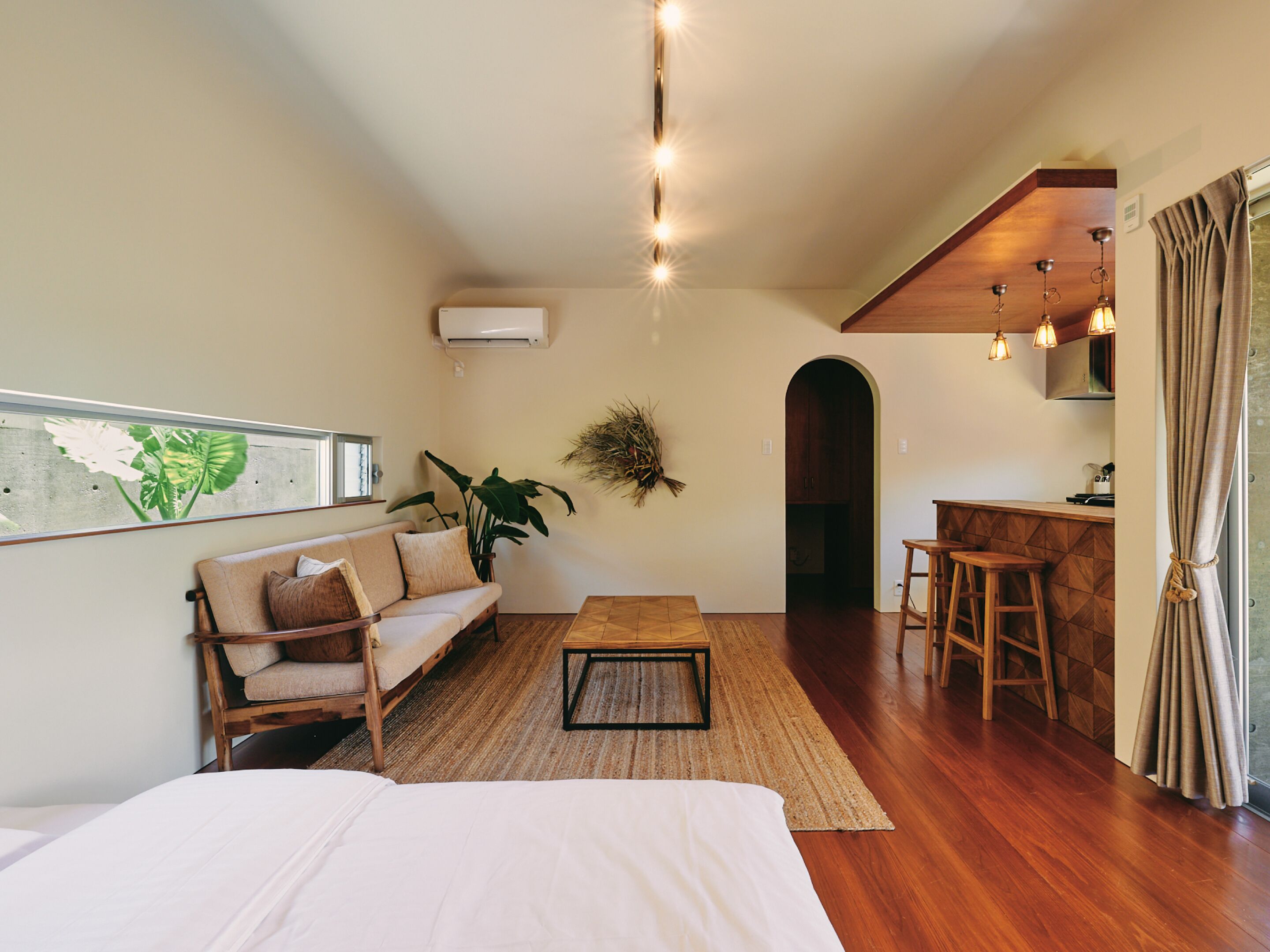 A cozy room with a bed, a sofa, a coffee table, and a kitchen area with stools.