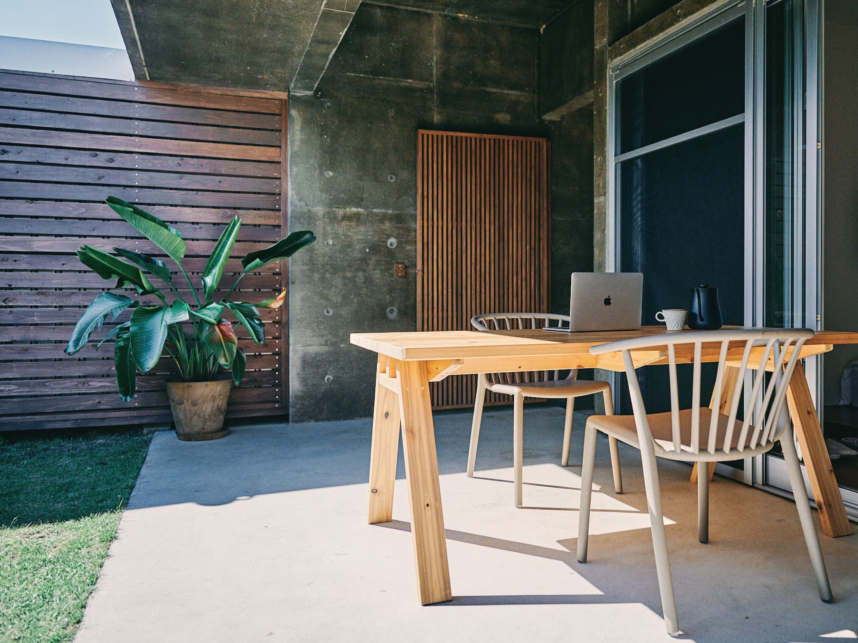 Une table en bois avec des chaises, un ordinateur portable et une plante en pot, le tout dans un décor extérieur moderne.
