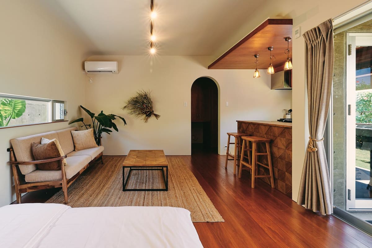 A cozy room with a bed, a sofa, a small table, and a kitchen area with stools.