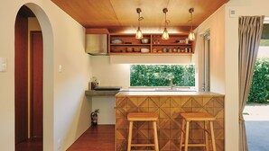 A compact kitchen with a wooden countertop, two stools, and pendant lighting. - IMAGINE OKINAWA (Nakijin)