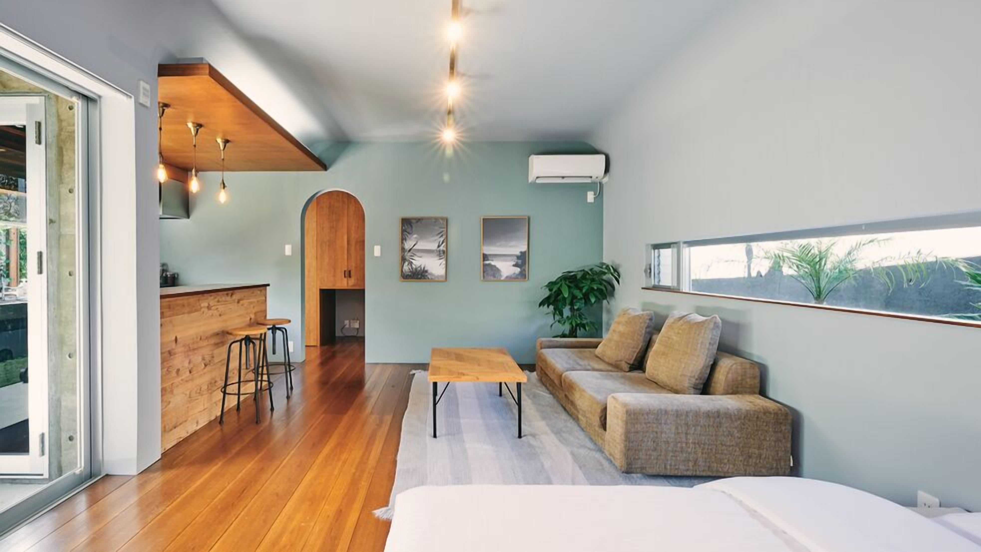 An open-plan living space with a kitchen, a sofa set, a dining area, and a large window.