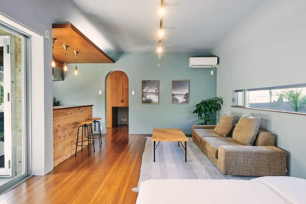 An open-plan living space with a kitchen, a sofa set, a dining area, and a large window.